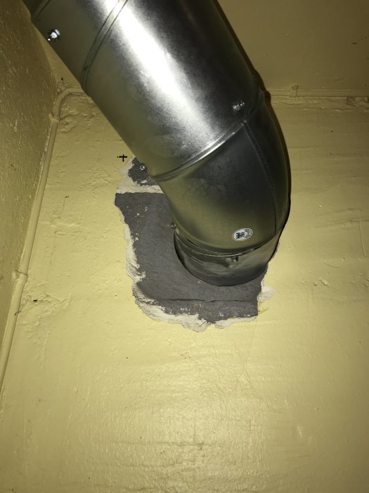 Ventilationsrör genom gult vägguttag med synlig skada och behov av reparation.