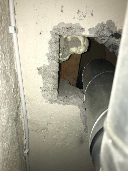 Genomföring i lättbetongvägg med synlig rörledning och byggskum runt kanten.