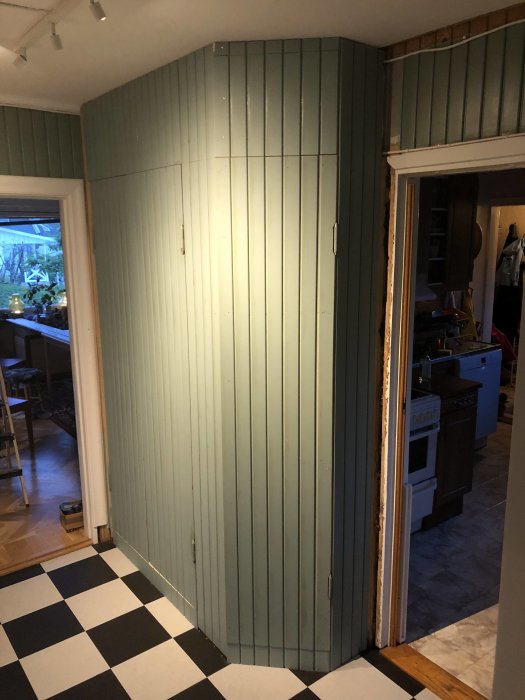 Renoverat hörnskåp i grönt med väggpanel, omålad dörrkarm och schackrutigt golv.