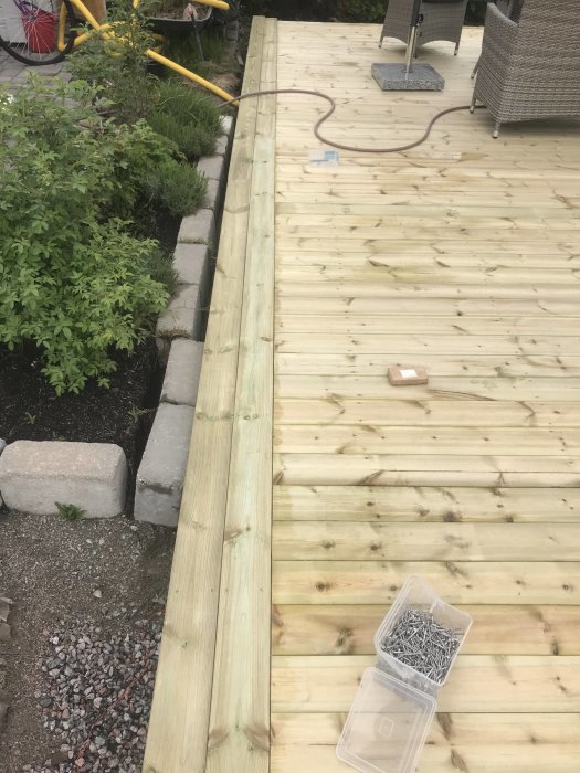 Nylagt trätrall för en altan med verktyg och skruvar synliga, gränsande till en trädgård.