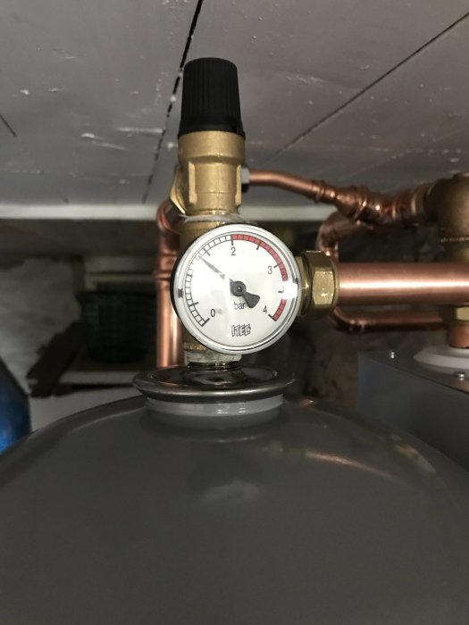 Manometer visar ca 0,7 bar på en varmvattenberedares trycksystem i en källare.