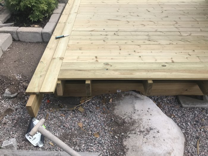 En ofärdig träaltan med synliga reglar och verktyg på grusunderlag.