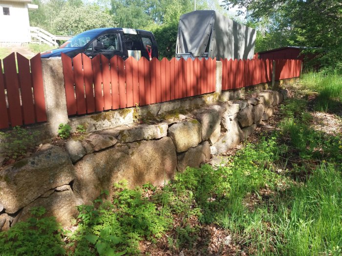 Stenmur där stora stenblock sticker upp genom marken med gräsmatta och staket i bakgrunden.