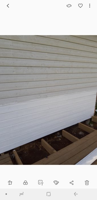 Nyinstallerad vit träpanel på en byggnads sida redo för målning med synlig träramkonstruktion nedtill.