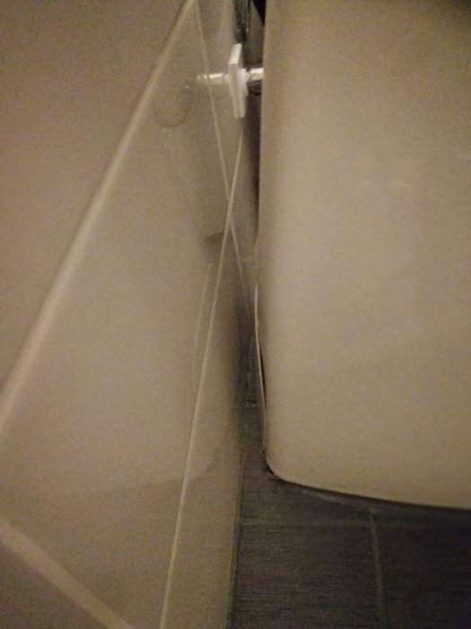 Trångt utrymme mellan badkarsida och vägg med synlig röranslutning.