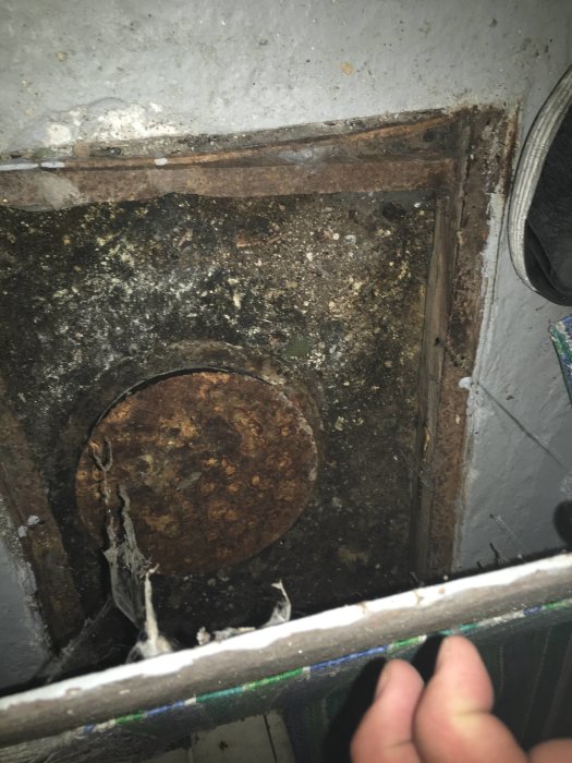 Rostigt lock i ett betonggolv med synlig mjuk jordliknande yta undertill i en källare.