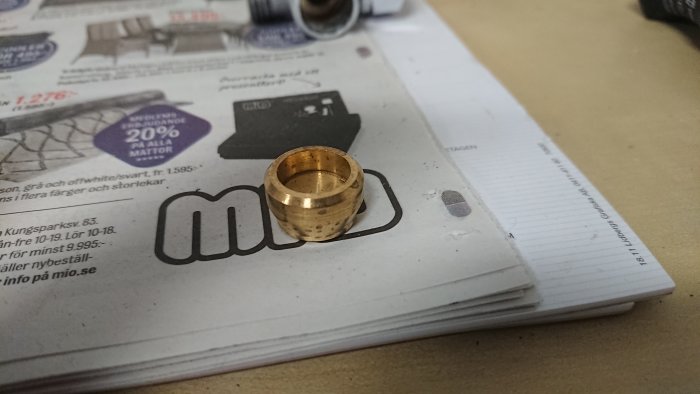 En omärkt mässingsplugg ligger på en öppnad tidning, monteringsriktning okänd.