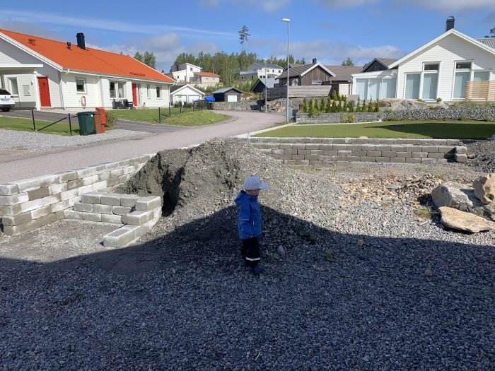 Barn framför grävd grund till byggprojekt med stödmur och grannhus i bakgrunden.