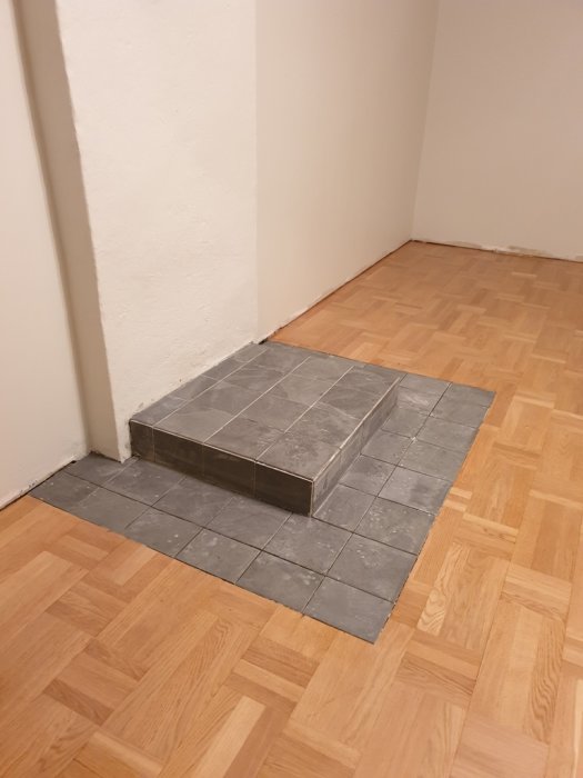 Golvgips lagt på en del av ett trägolv, bild visar grå kakelplattor och ofogade skarvar.