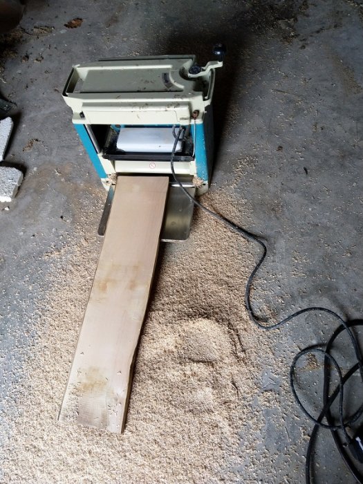 Okantat trä som genomgår en grovhyvling med elektrisk planhyvel på betonggolv.