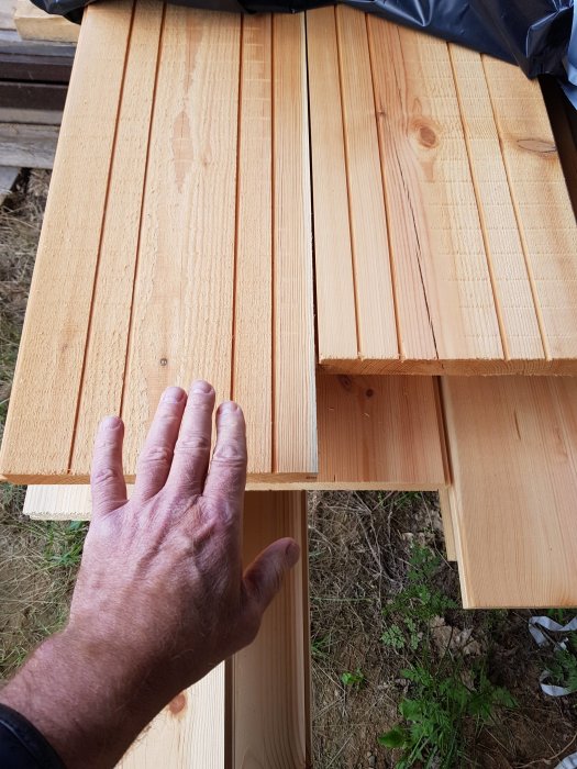 Hand som inspekterar breda träplankor för golvläggning som har torkat på sågverk.