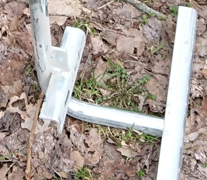 Närbild av en metallkonstruktion på marken bland löv och smågrenar, med tecken på tveksam hållbarhet.