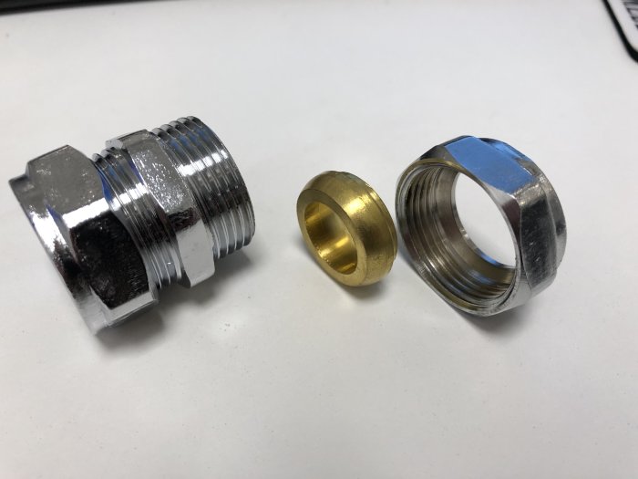Två olika metallpluggar på ett bord, en silverfärgad med gängor och en guldfärgad med slät yttre del.
