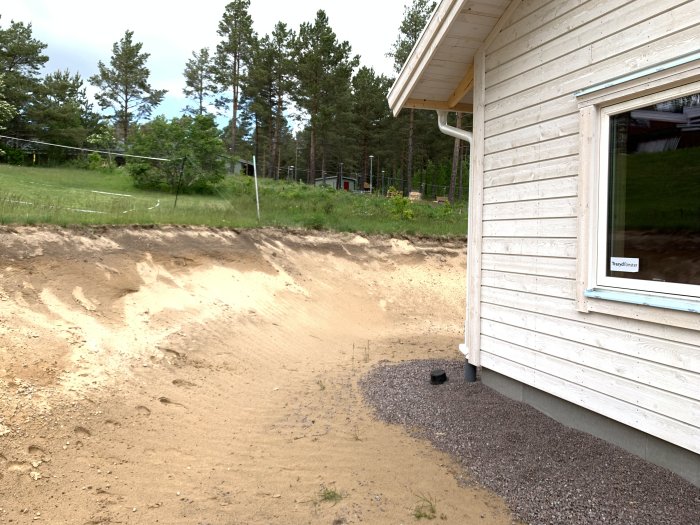 Brant sandig slänt nära en husvägg med synlig höjdskillnad och spår av erosion.