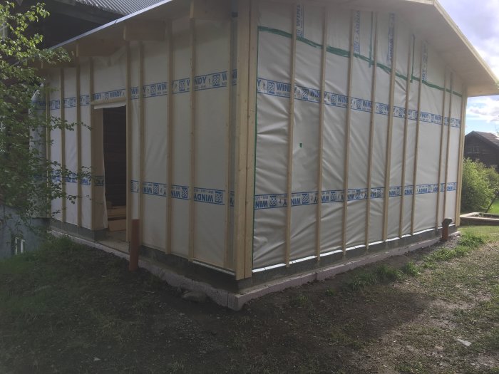 Nybyggd stomme till ett hus med vindskyddspapp som är delvis monterat.