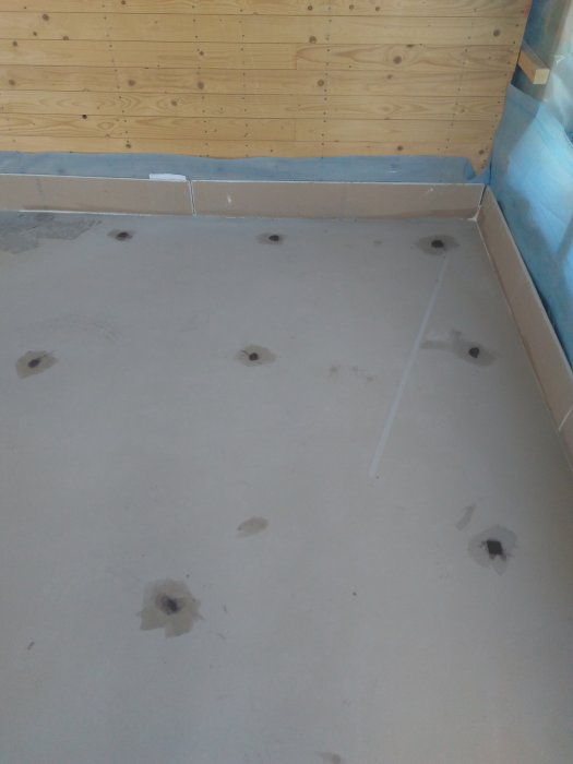 Ett betonggolv med ojämnheter och flera små högar av Ardex A45, redo för vidare flytspackling.