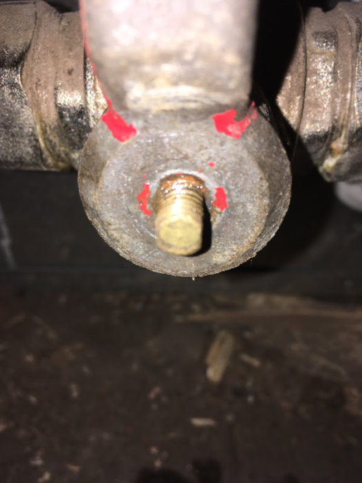 Närbild av en oxiderad ventil utan handtag, synlig skruv och ventilstam, med röda markeringar runt skruven.