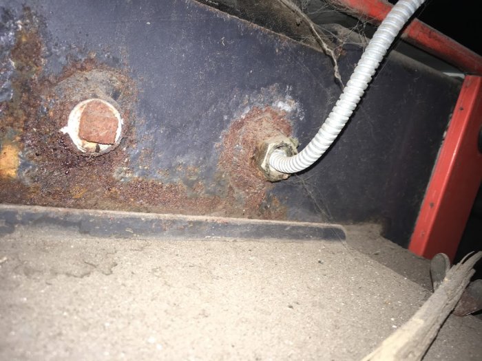 Rökgastermostatens koppling vid en rostig panna med flätat skyddsrör och tom installationsöppning.