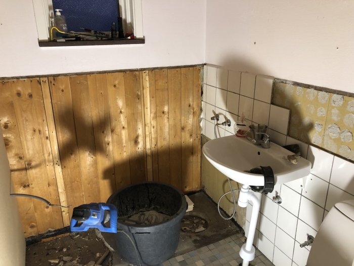 Pågående renovering av ett badrum med trävägg under rivning och ogjort kakelarbete.