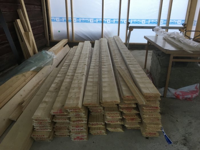 Trav av ny inburad timmerpanel ligger staplad inomhus.