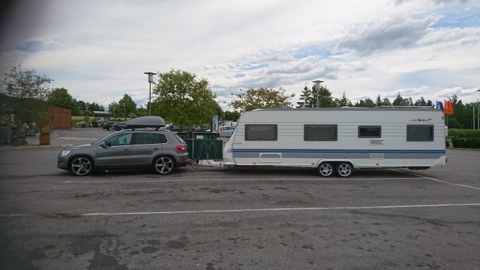 VW Tiguan med takbox som drar en vit husvagn parkerad på en parkering.