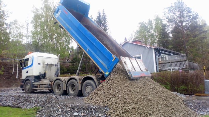 Lastbil tömmer grus för markförstärkning nära ett hus med terrass.