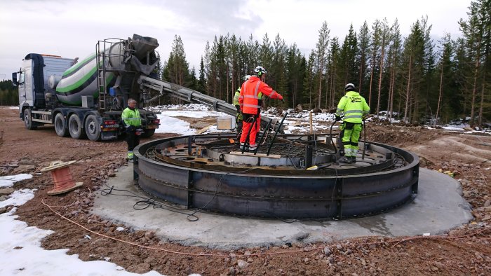 Arbetare vid gjutning av fundament med betongbil och gjutformar på en byggarbetsplats.