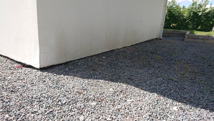 Hörnet av en vit putsad byggnad där putsen slutar nära grusmarken, utan list på avslutet.
