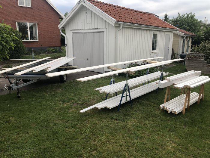 Nymålade balkongräcken ligger utspridda för torkning på gräsmattan framför vit garagebyggnad.