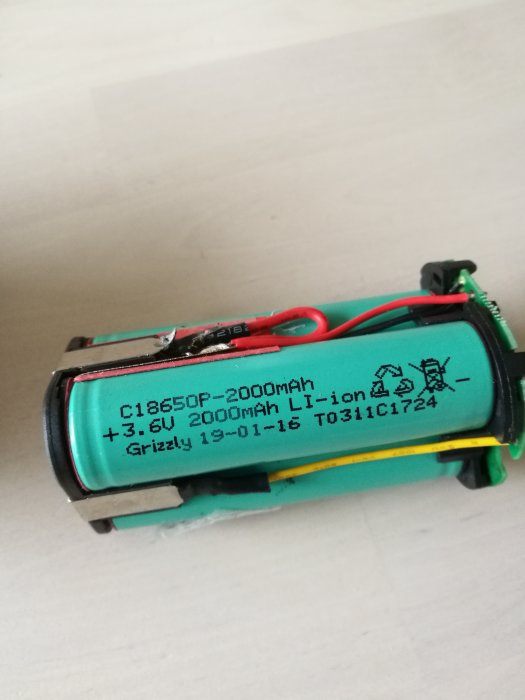 Öppnat litet batteri som visar en blå cell och delar av kretskortet, märkt med specifikationer "C18650P-2000mAh +3.6V".