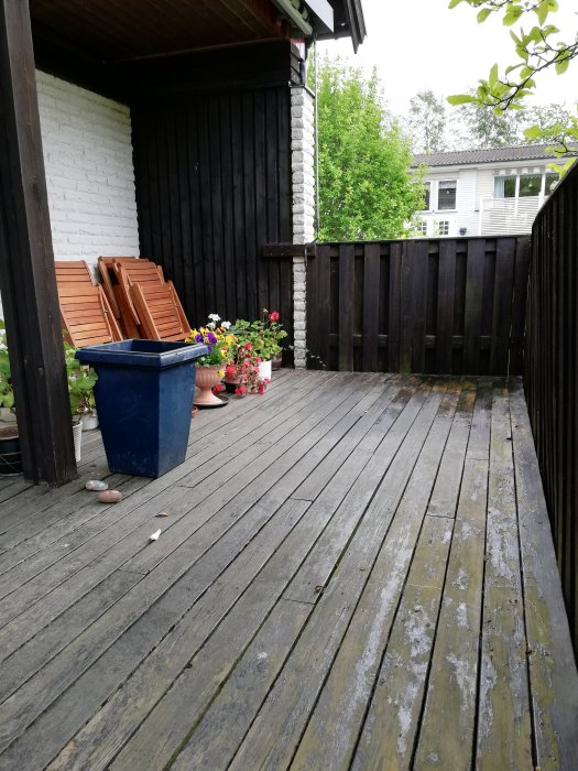 En träaltan vid ett hus med sittmöbler och blomkrukor, redo för utbyggnad.