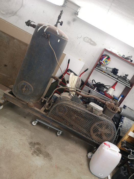 Åldrad industriell maskin uppsatt på hjul med tank och kopplingar, placerad i ett garage.