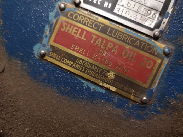 Gammal smörjningsplåt på maskin med Shell Talpa Oil 20-information, rost och blå färg i bakgrunden.
