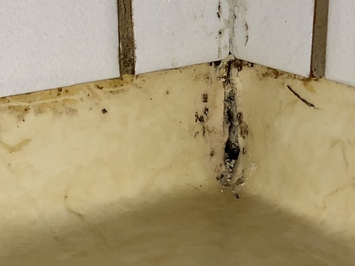 Skadat hörn i badrum med mögel och rester efter borttaget gammalt silicon, som visar tecken på fuktproblem.