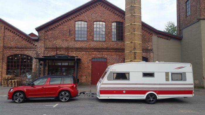Röd Skoda Yeti kopplad till en vit husvagn parkerad framför en tegelbyggnad.