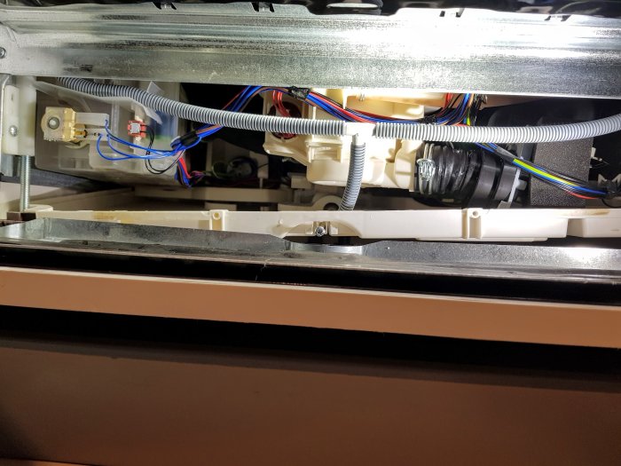 Nedre delen av en diskmaskin med synlig avloppspump och bälge samt kablar och slangar.