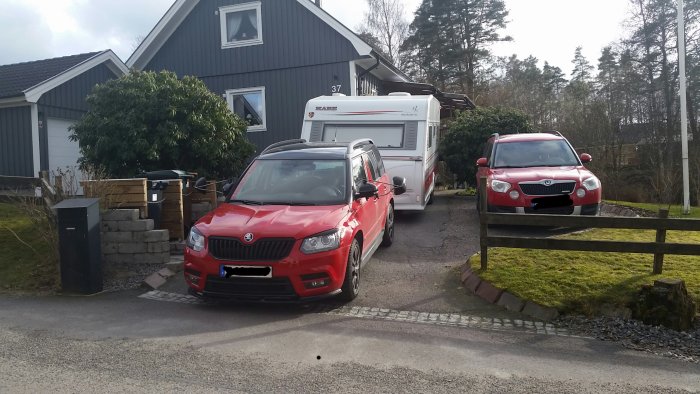 Röd bil backar en husvagn med registreringsskylten censurerad, framför ett hus.
