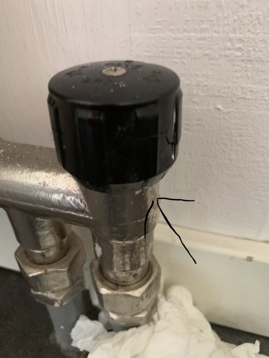 Svart termostat på radiator med synligt läckage vid anslutningen, markerat med en svart pil.