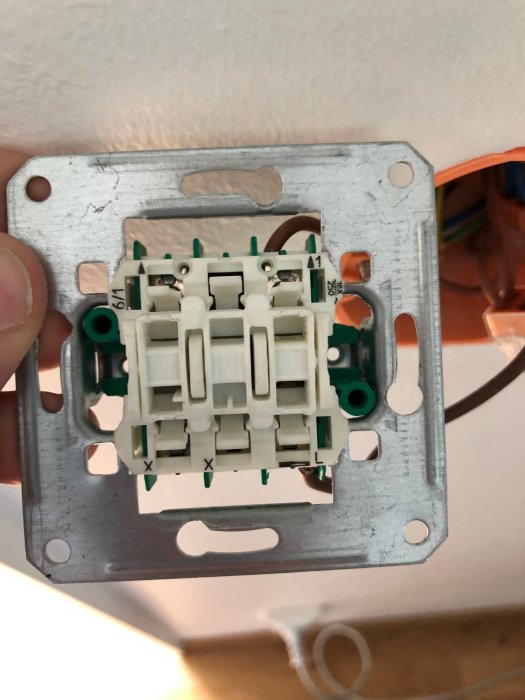 En hand håller en demonterad elektrisk strömbrytare med ledningar och anslutningspunkter synliga.