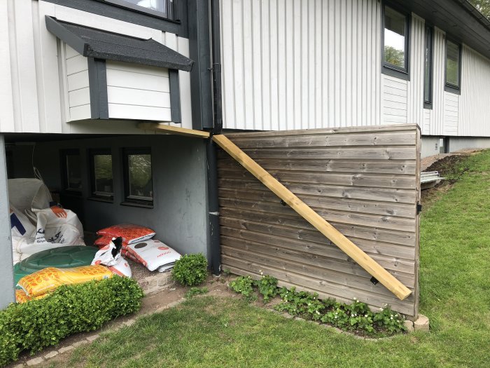 Nybyggt staket vid hus med trappsteg i trä riktade mot en dörr och en påbörjad trätrappa.