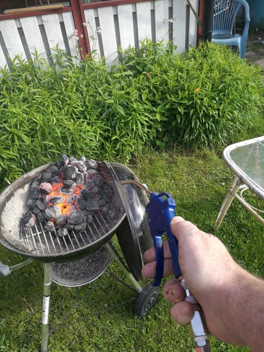 En person blåser med en handhållen blåsbälg på glödande kol i en utomhusgrill för att snabba på processen.