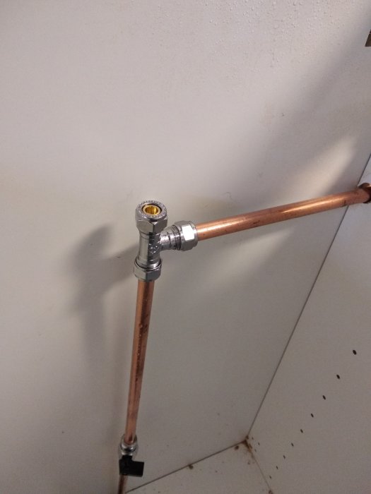 Kopparledning med nyinstallerad koppling och avstängningsventil mot en vägg.