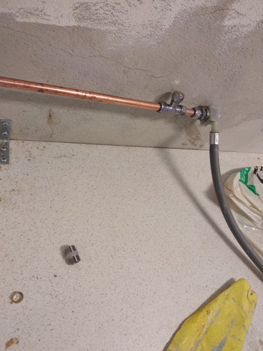 Kopparledning med kopplingar och en lös del på ett smutsigt golv i ett pågående VVS-projekt.