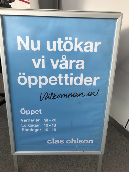 Blå skylt som annonserar utökade öppettider för en butik med texten "Nu utökar vi våra öppettider" och öppettider listade för olika dagar.