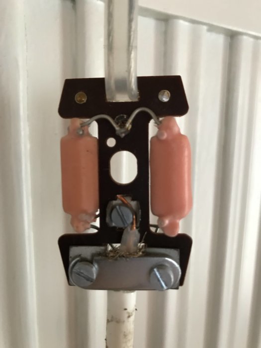 En sliten antennsignalssplitter monterad på en vit kabel, med synliga skador och tecken på åldring.