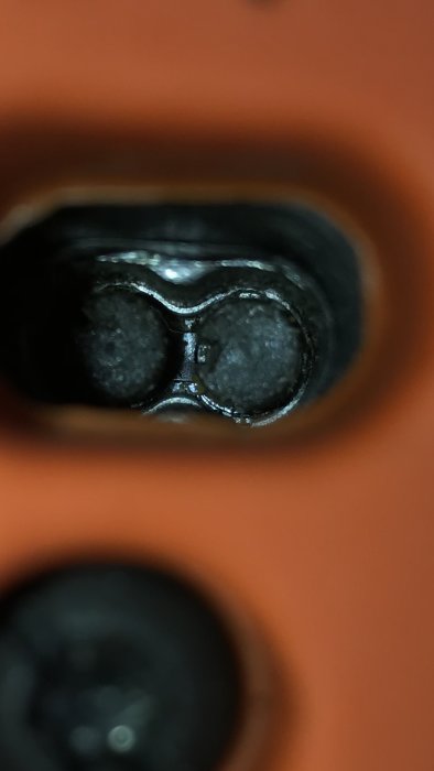 Närbild av en eluttagshålighet med två slitsar och jordningsöppning i en orange vägg.