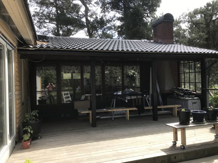 Träterrass med takstolar som vilar på pelare, intill en västkuststuga med synlig taköverhäng.