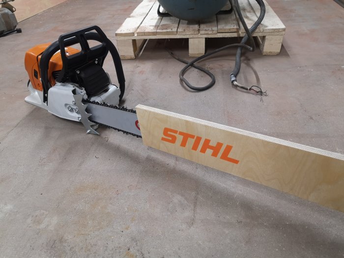 Motorsåg av märket STIHL intill en träplanka på en verkstadsgolv.