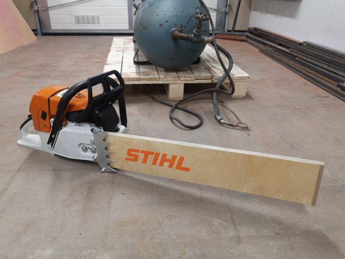 En motorsåg med långt svärd av märket STIHL på ett verkstadsgolv.