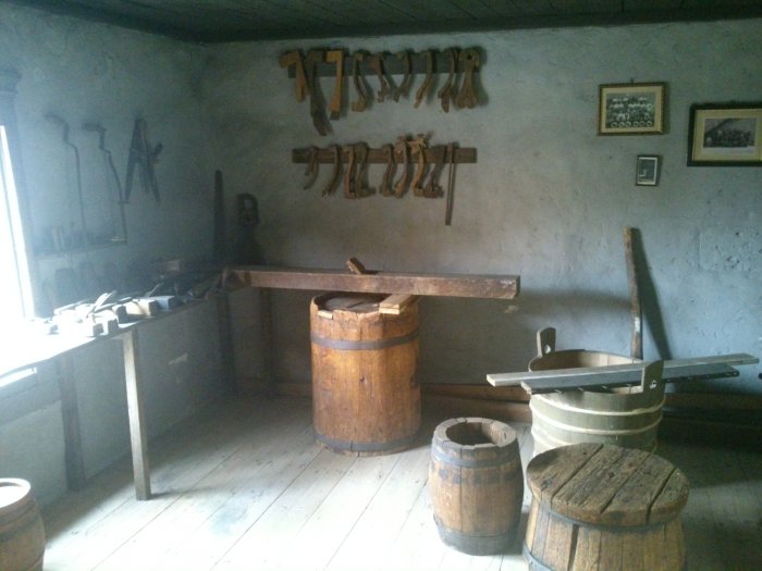 Gammalt snickarverktyg, troligen en hyvel, står på en trä tunna i ett historiskt hantverksmuseum.